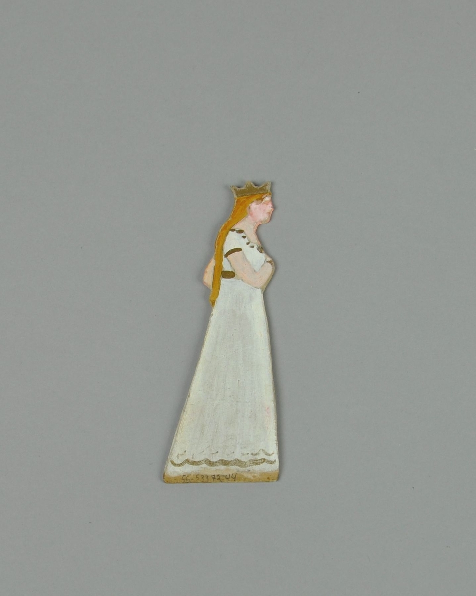 Figur av papp. Figuren forestiller stående dame i sideprofil, med krone og hvit kjole. Figuren er malt på begge sider.
