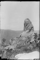 Ung jente sittende på stein med utsikt mot fjell.