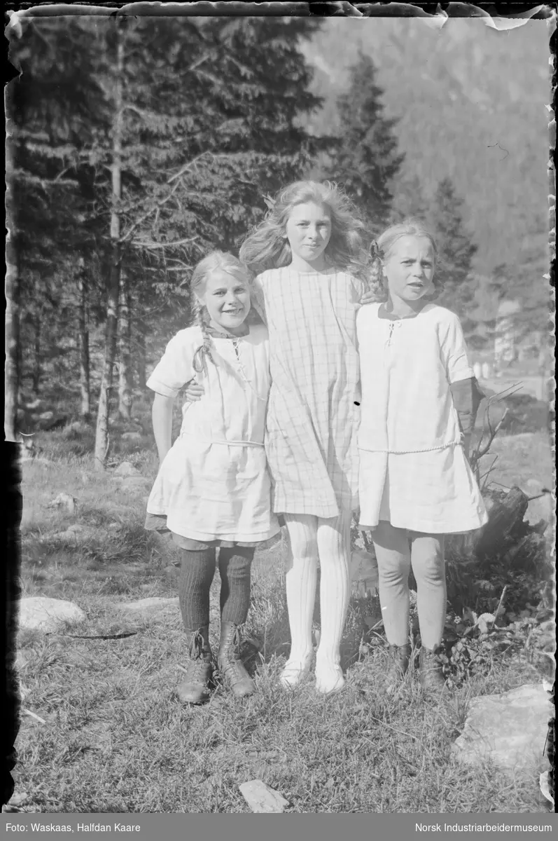 Tre unge jenter i kjoler stående utendørs.