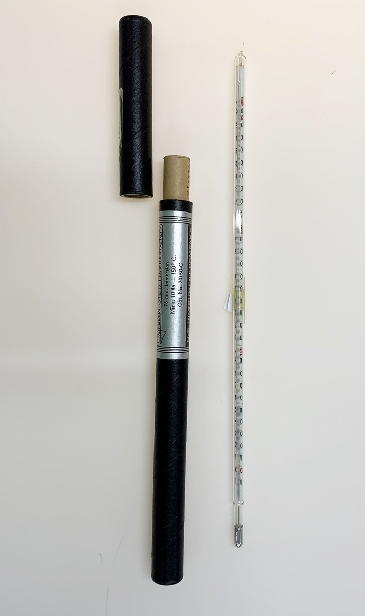 Termometer av glas med svart sifferskala på plast. Skala från -10 C till + 300 C. Tillhörande pappfodral är äldre än termometern och var ursprungligen avsedd för en annan termometer.