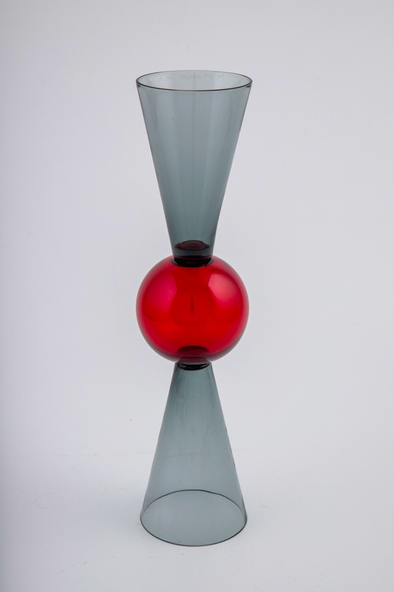 Vinglass utført i farget gjennomskinnelig glass. Røkfarget kupa og fot som er konisk utformet, og smalner mot glassets midtparti som består av en rødfarget kule. Dermed kan begge sidene fungere som fot og klokke.