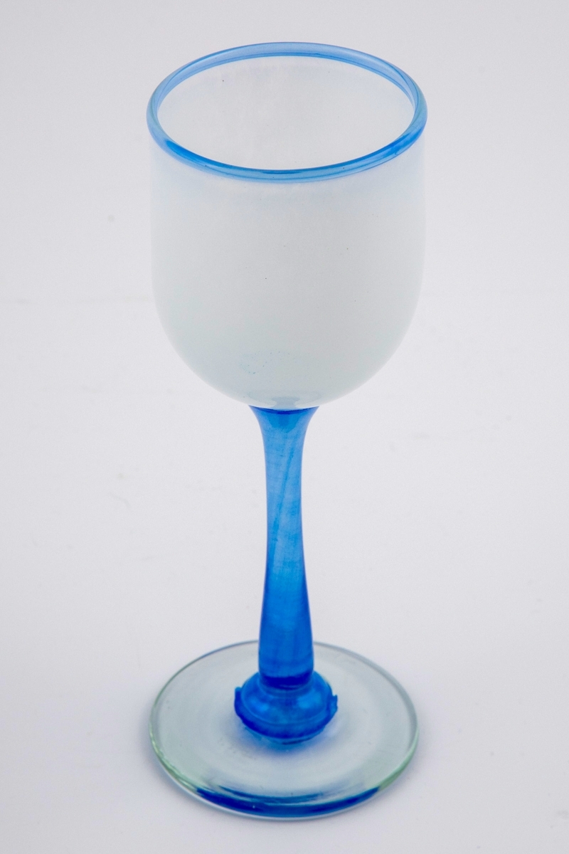 Vinglass med hvit halvgjennomskinnelig kupa. Munningen er markert med en blålig rand. Stetten er utført i klart blåfarget glass, og hviler på en sirkulær fot med puntemerke.
