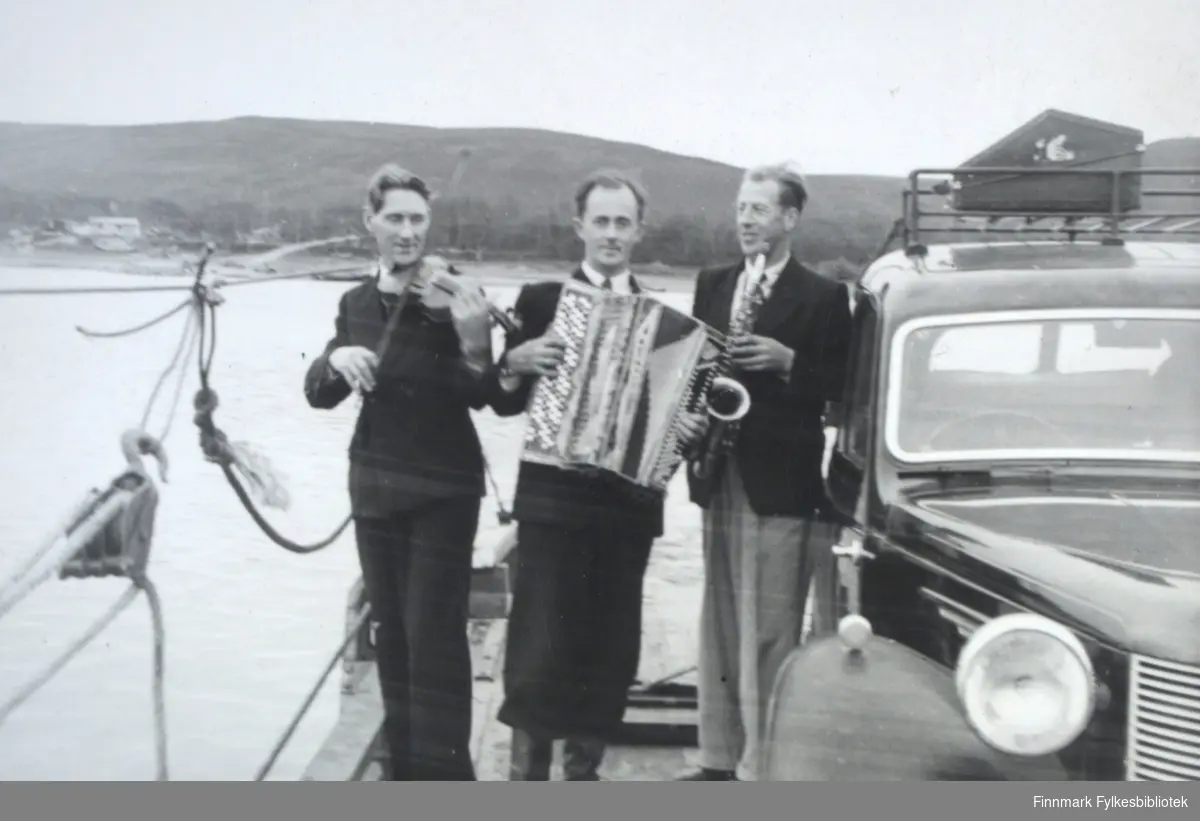 Fra venstre: Ole Johnsen (fiolin), Ivar Sælø (trekkspill) og Edmund Jankila (saxofon). Et sted langs Tanaelva med ferge, muligens i Seida, på 1950-tallet. Ivar Sæløs bil Austin A10 til høyre.