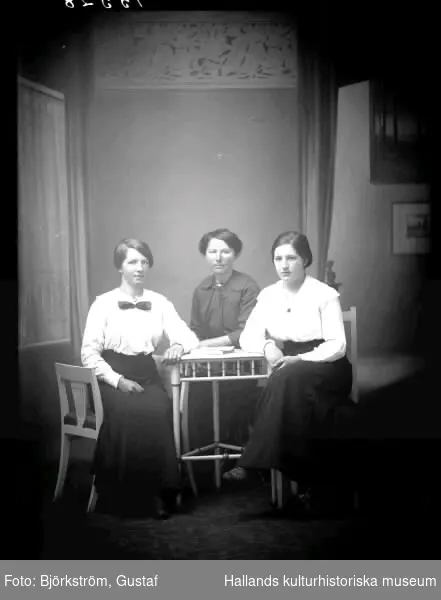 Ateljébild av tre unga kvinnor vid ett bord. Beställare: Alma Gunnarsson, Svenstorp 2, Derome. Se även bildnr GB2_4983.