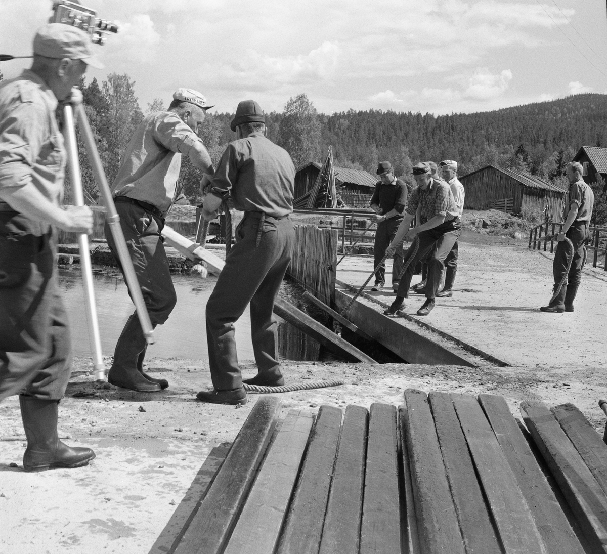 Mann med filmkamera driver dokumentasjon av fløtinga ved Haldammen på Våler Finnskog i Hedmark i 1969. Her sprettes nåledammen. Flisavassdraget. Elva Flisa.