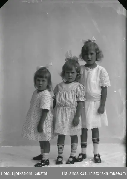 Ateljébild av tre små flickor i helfigur, troligen systrar. Beställare: Fröken  Laurizohn.