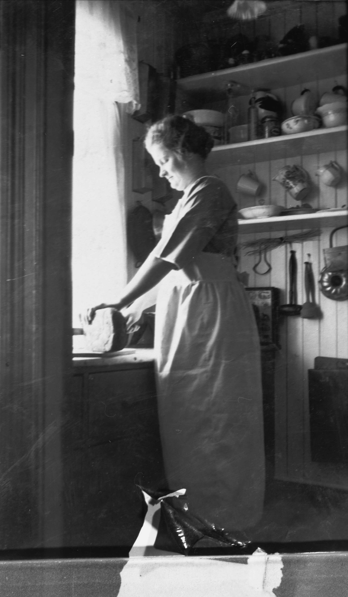 Portrett av kvinne som skjærer brød på et kjøkken.