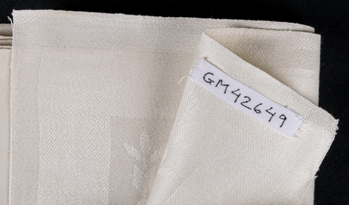 Oklippt, maskinvävd bordduksväv av hellinne, vit med vävda mönster, damast. Tillverkad vid Torsåkers linnefabriks aktiebolag.
Försedd med pappersetiketter med tillverkarens emblem