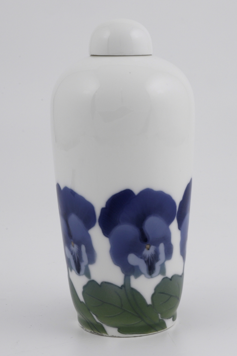 Vase i støpt porselen med tilhørende halvkuleformet lokk. Nedre del av korpus er dekorert med en bord av stemorsblomster i underglasurmaling. Liten sirkulær munning.