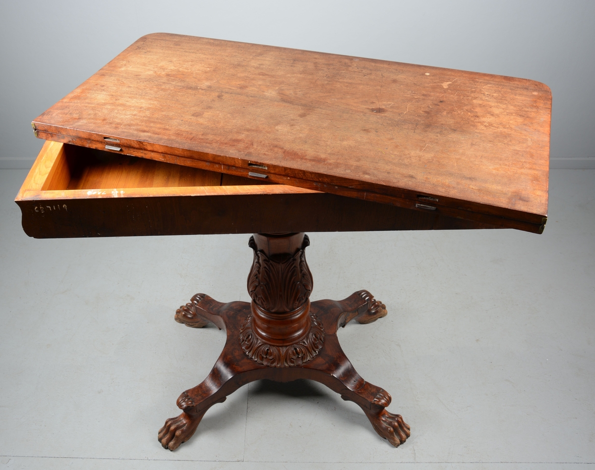 Spillebord med todelt, sammenleggbar og svingbar plate. Kraftig, dreid søylefot ornamentert med bladverk på understell med fire løveføtter.