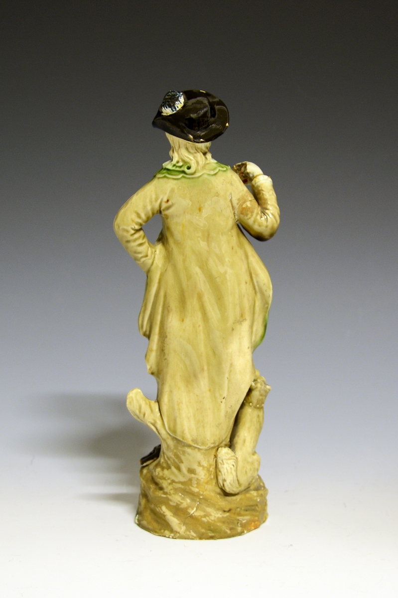 Kvinnefigur av fajanse, hvit glasur med håndmalte polykrome detaljer. Spiller på en tamburin som hun holder over venstre skulder.