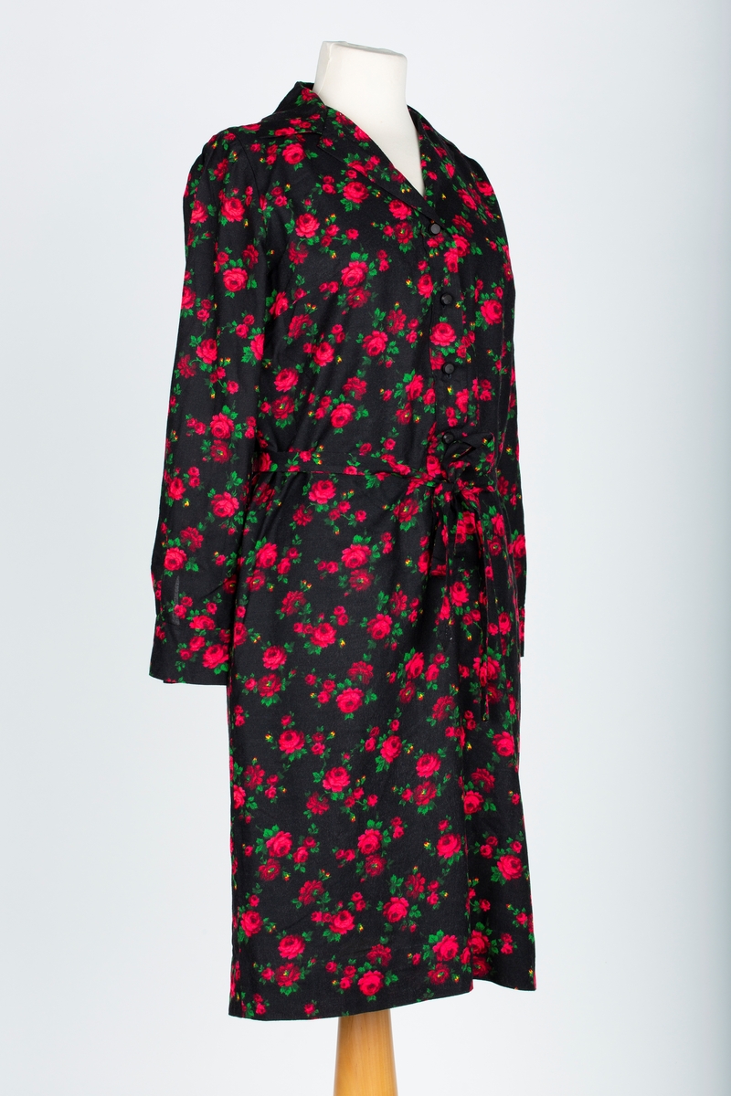 A: Kjole
Skjorteblusekjole. Lange ermer med mansjett, rødt og grønt rosemønster på sort bunn. Stolpeknapping i halsen, Brystsnitt. rette sider. 

B: Knyttebelte

Kjolen sydd av mor, Ella Viktoria Hagen.