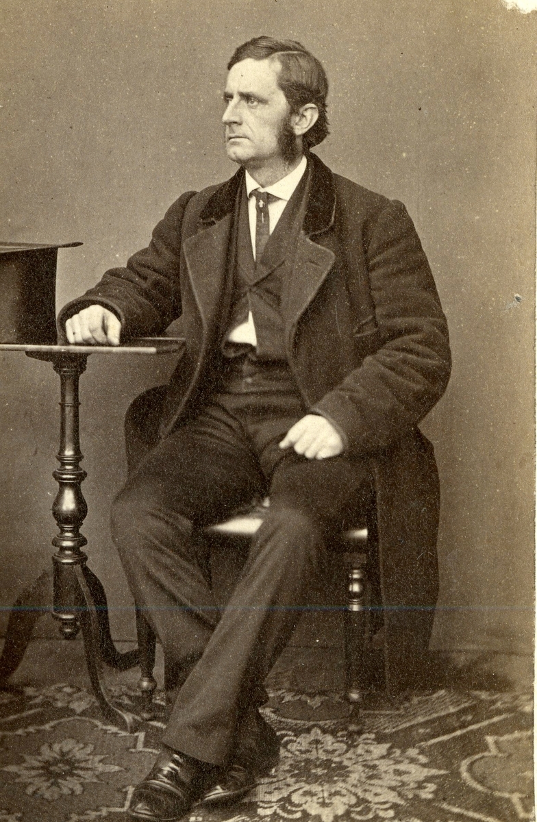 Anton Holmboe sittende, flosshatt på bord. 1863