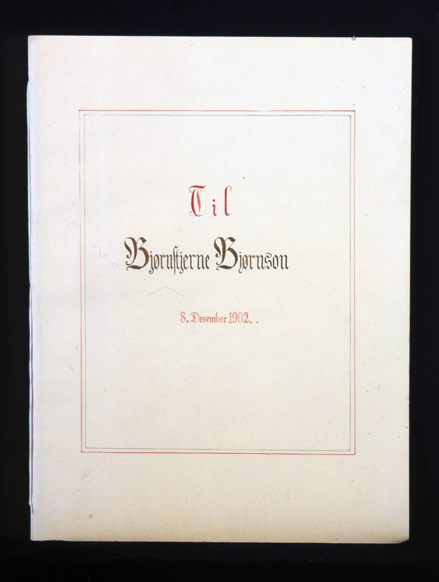 Adresse med mappe i mørkebrunt skinn med gullskrift på forsiden. Løse doble blad med mange hilsener i gullrammer. Adressen er skrevet med gotiske bokstaver i svart, rødt og gull.