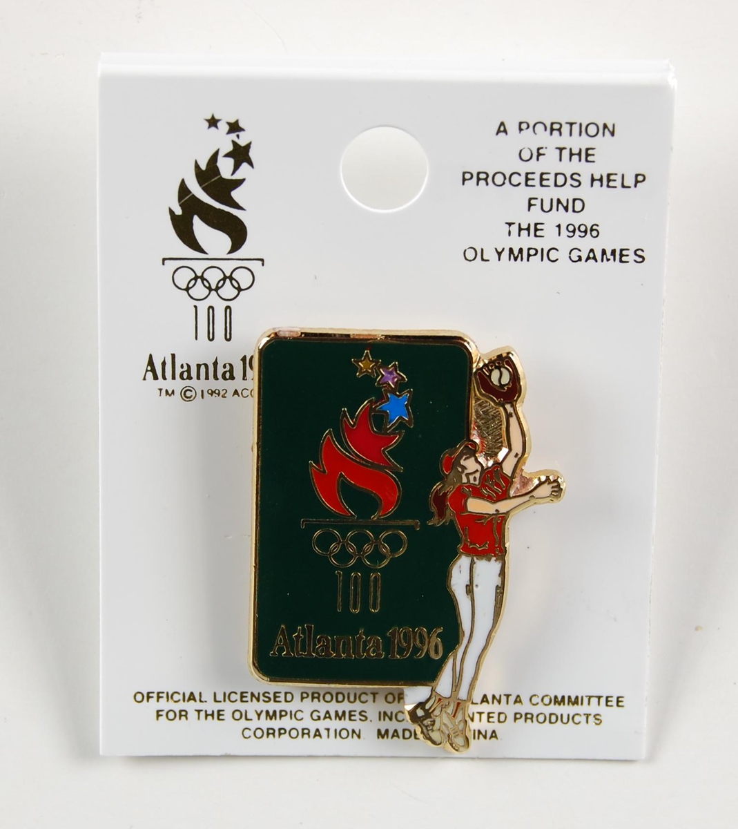 Grønn og gullfarget pins. På pinsen er det en flerfarget logo for de olympiske leker i Atlanta i 1996 og et motiv av en kvinnelig softball-spiller. Motivet preger også pinsens form. Pinsen sitter festet til en liten plate av papp.