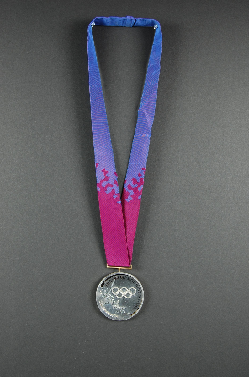 Rund medalje i valør sølv. I dekoren på den ene siden er det et piktogram av en alpinist, og motivet er hentet fra LOOCs designprogram. Det er også stemplet logo for de olympiske leker på Lillehammer i 1994. På den andre siden inngår de olympiske ringene som en del av dekoren.
