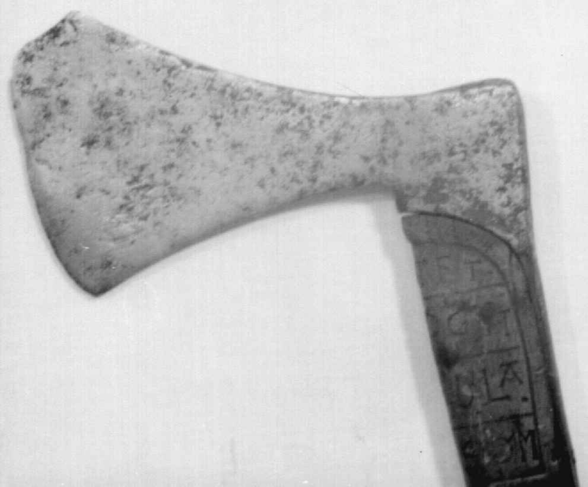 Asymmetrisk økseblad, sammensveiset med overliggende jernskinne.
Fremre øksebladspiss brukket.
Rikt dekorert skaft med flettet rutemotiv. Innskripsjon på øvre del av skaftet (se Påført tekst)
