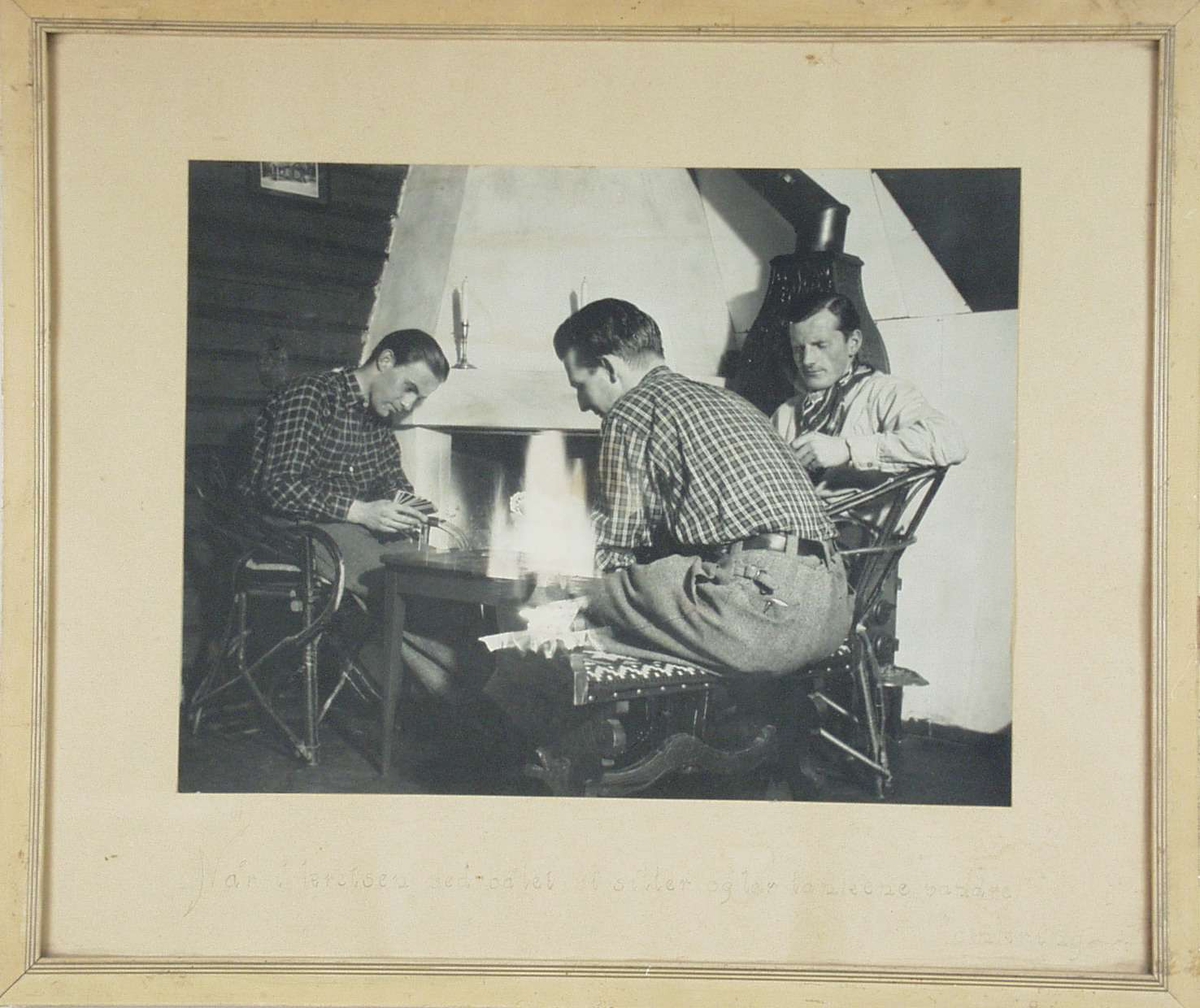 Tre menn ved peisen som spiller kort.