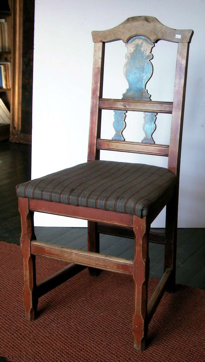 Spisestuestol med pute. Stolen er rød- og blåmalt. Malingen er nedslitt. Trekket er husflidsaktig og har brede grå striper med smale striper i bondeblått, rødt og gult.