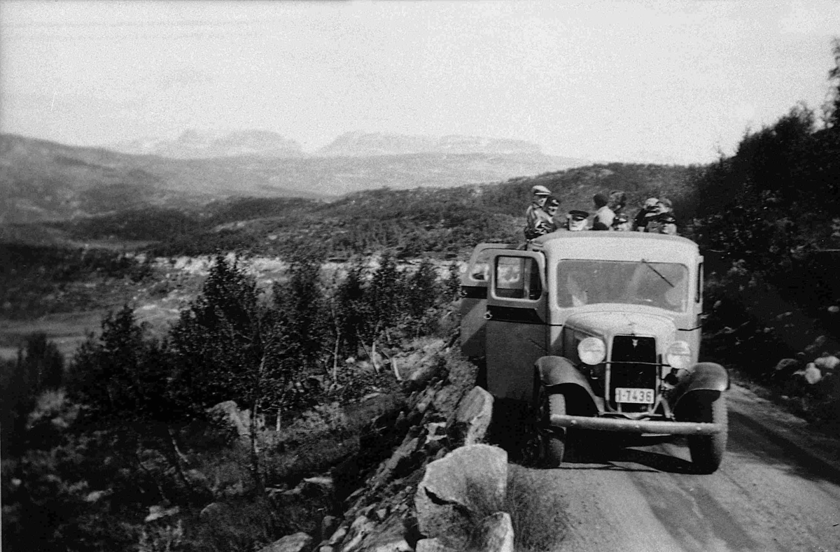 Busstur. Bussen er en Ford V8 1933-34-modell. Den ser ut til å ha reg.nr. I-7436. Høyeste nr. i Norges Bilbok 1935 (utkom på vårparten 35?) var I-7403. Legg merke til  åpen bakdør, og at taktrekket er rullet tilbake ("solskinnsbuss").