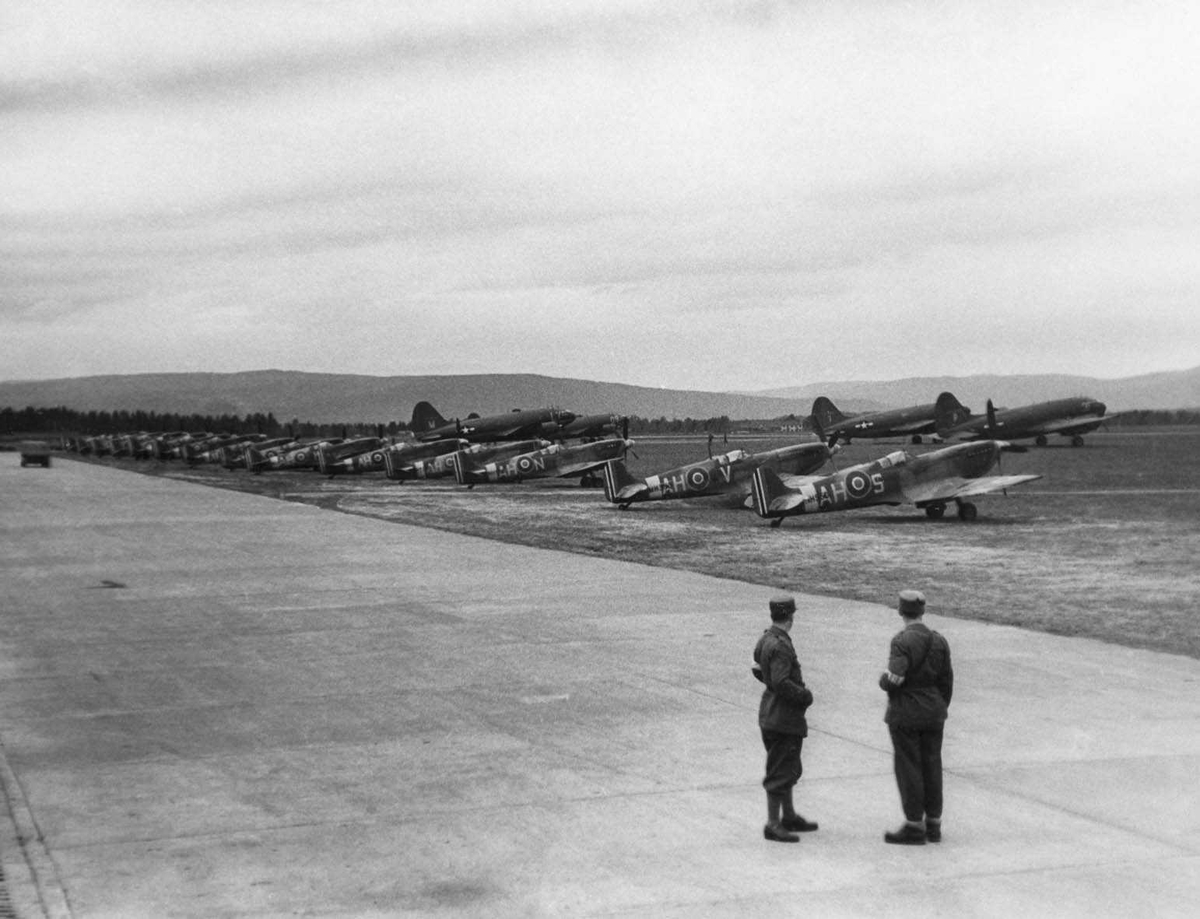 Gardemoen. Amerikanerne har flyutstilling. Juni / juli 1945. Flyene står oppstilt ved rulle banen, to menn i uniform står og ser på.
