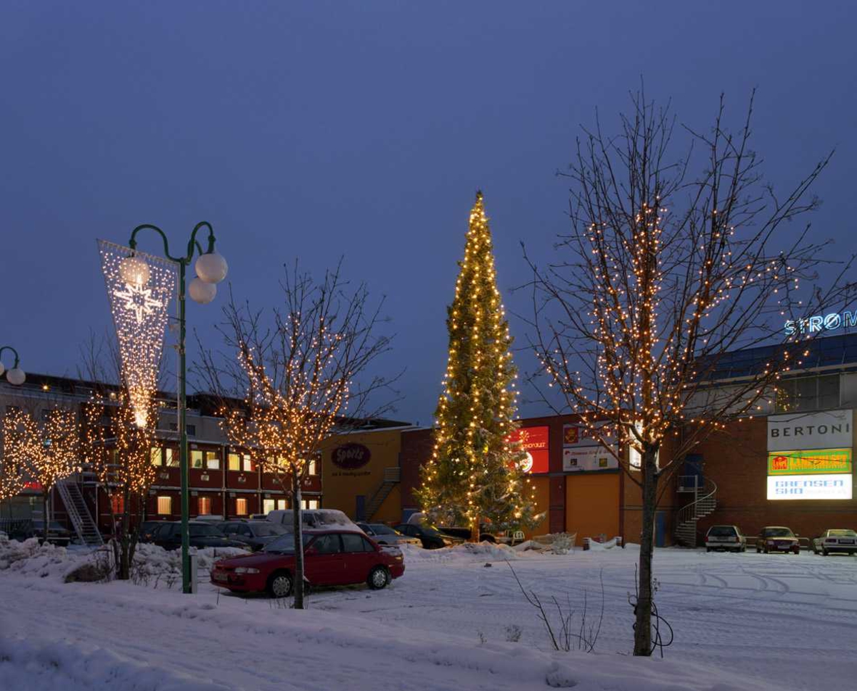 Julebelysning.

Juletre på parkeringplads ved Strømmen Storsenter. hvite lyslenker som henger nedovertreet. Hvite lyslenker i treer langs veien og lys i kremmerhusform på lyktestolper