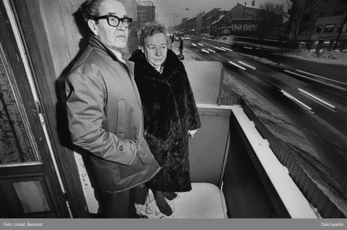 Eldre par på balkong ut mot trafikkert gate.Trafikkmiljø. Fotografiet er fra prosjektet og boka ''Oslo-bilder. En fotografisk dokumentasjon av bo og leveforhold i 1981 - 82''. Kontakt Samfoto ved ev. bestilling av kopier.