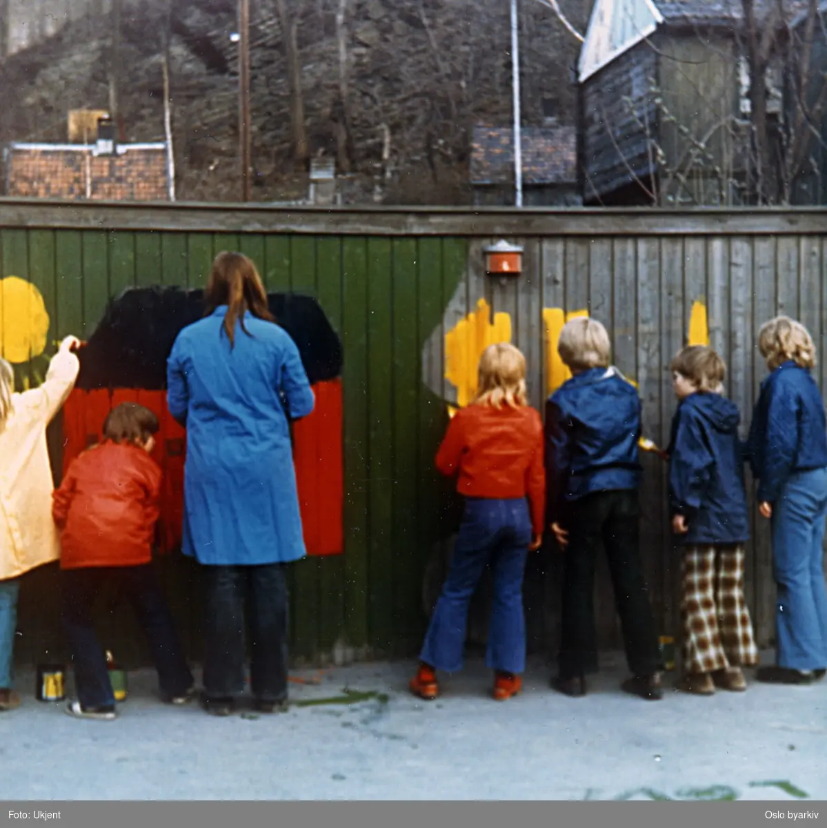 Barn fra Tøyen Juniorklubb dekorerer / maler på plankegjerde langs Kjølberggata. Trehusbebyggelse langs Brinken i bakgrunnen. Fra "Aksjon Spire 1973".