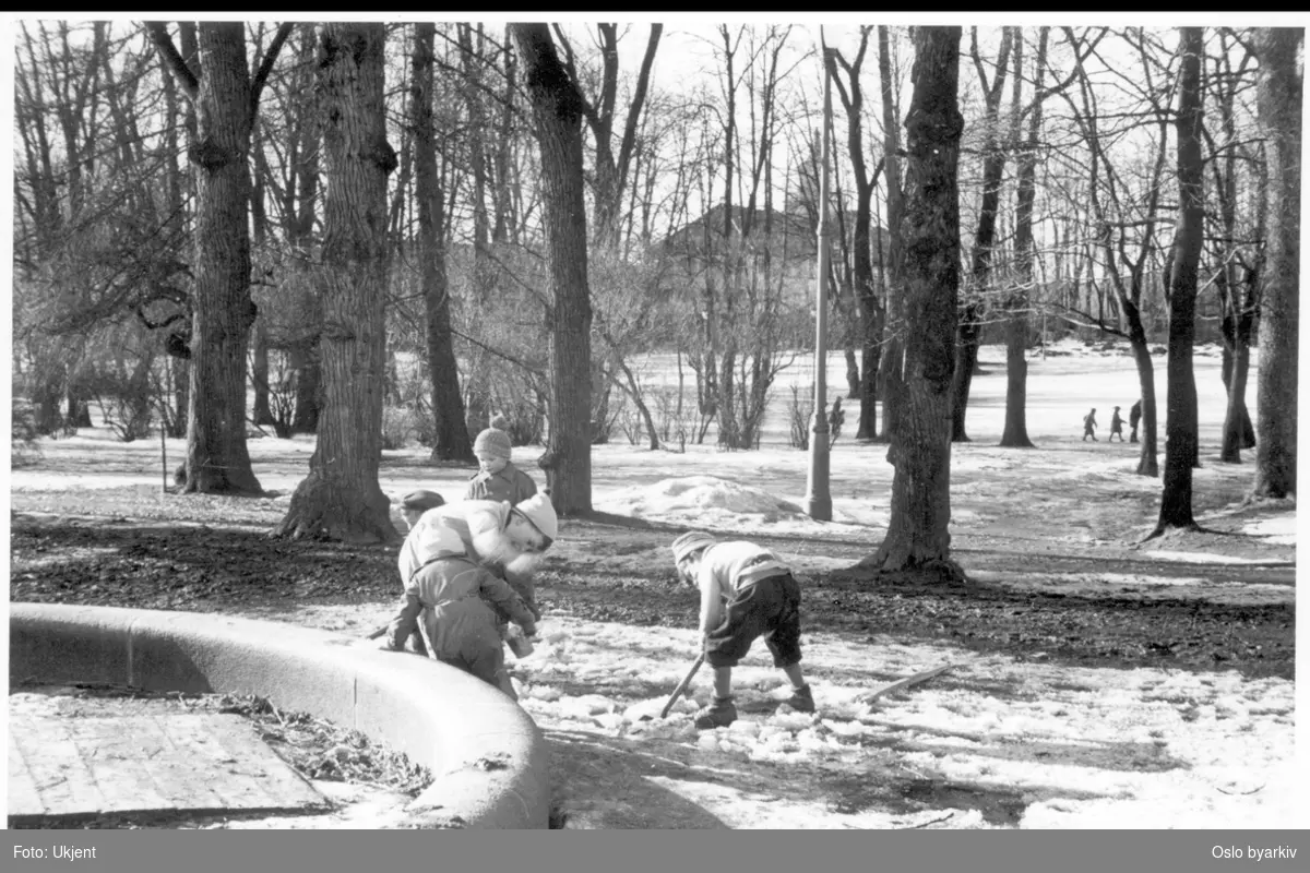 Vinter i Frognerparken. Lekende barn med spade på skarasnø ved lekeplassen sørøst i parken. Bildet tatt vestover mot Frogner Hovedgård (Bymuseet) i bakgrunnen. Vintertappet plaskedam.