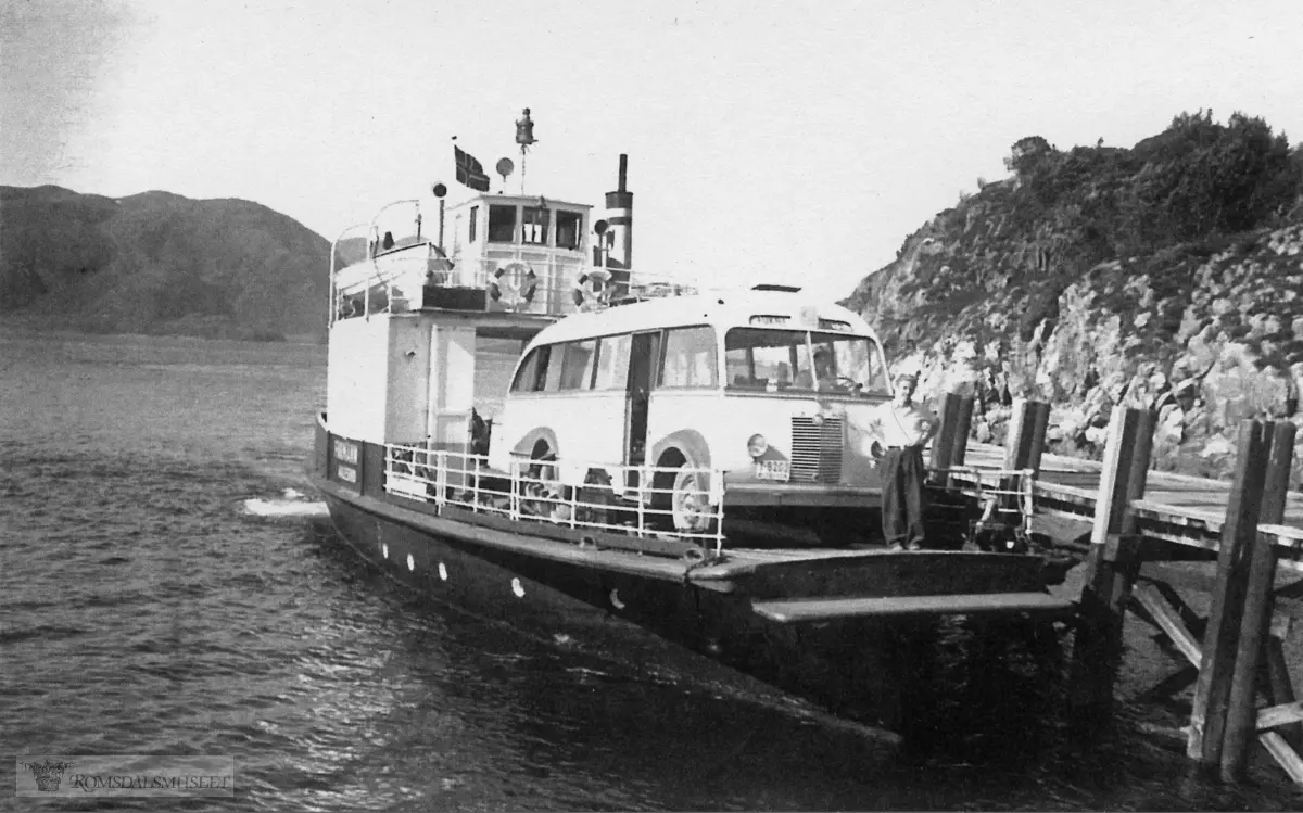 Hollingsholm fergekai. "Farman I".."Farman" var opprinnelig en båt bygd i 1920 og gikk i lokalruter Vatne - Midsund - Ålesund - Molde. I 1936-1937 ble den ombygd til bilferge som de neste 40 åra gikk i forskjellige fergesamband i Møre og Romsdal. 1948 - 1961 gikk den i ruta Aukra - Hollingsholm - Sundsbø (Otrøya). Bussen er antakelig T-8202. Aukra Auto fikk et tysk understell av merket Borgward, krigsmateriell, 1941-modell. Røvik Karosserifabrikk bygde på et busskarosseri med 29 seter. I juni 1949 ble bussen tatt i bruk i ruta Aukra - Molde.