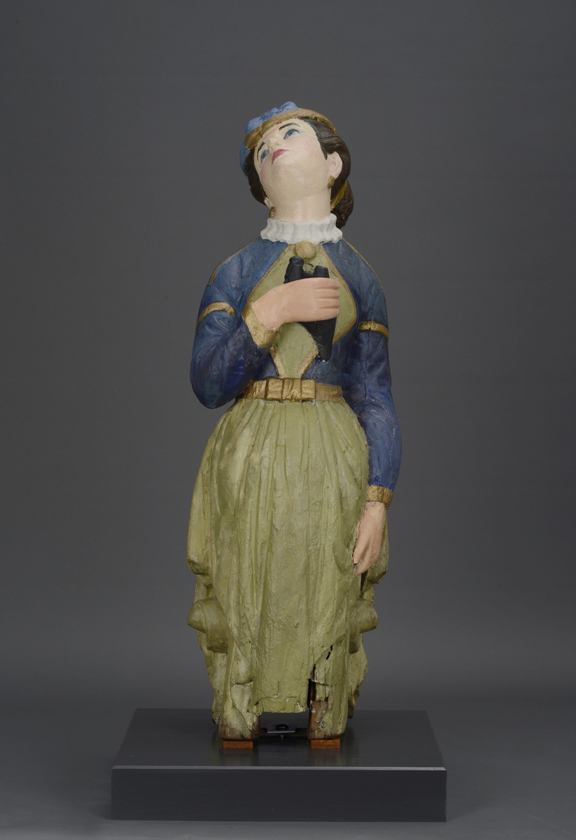 Utskjært kvinnefigur stående på en tresokkel med en kikkert i hånden.