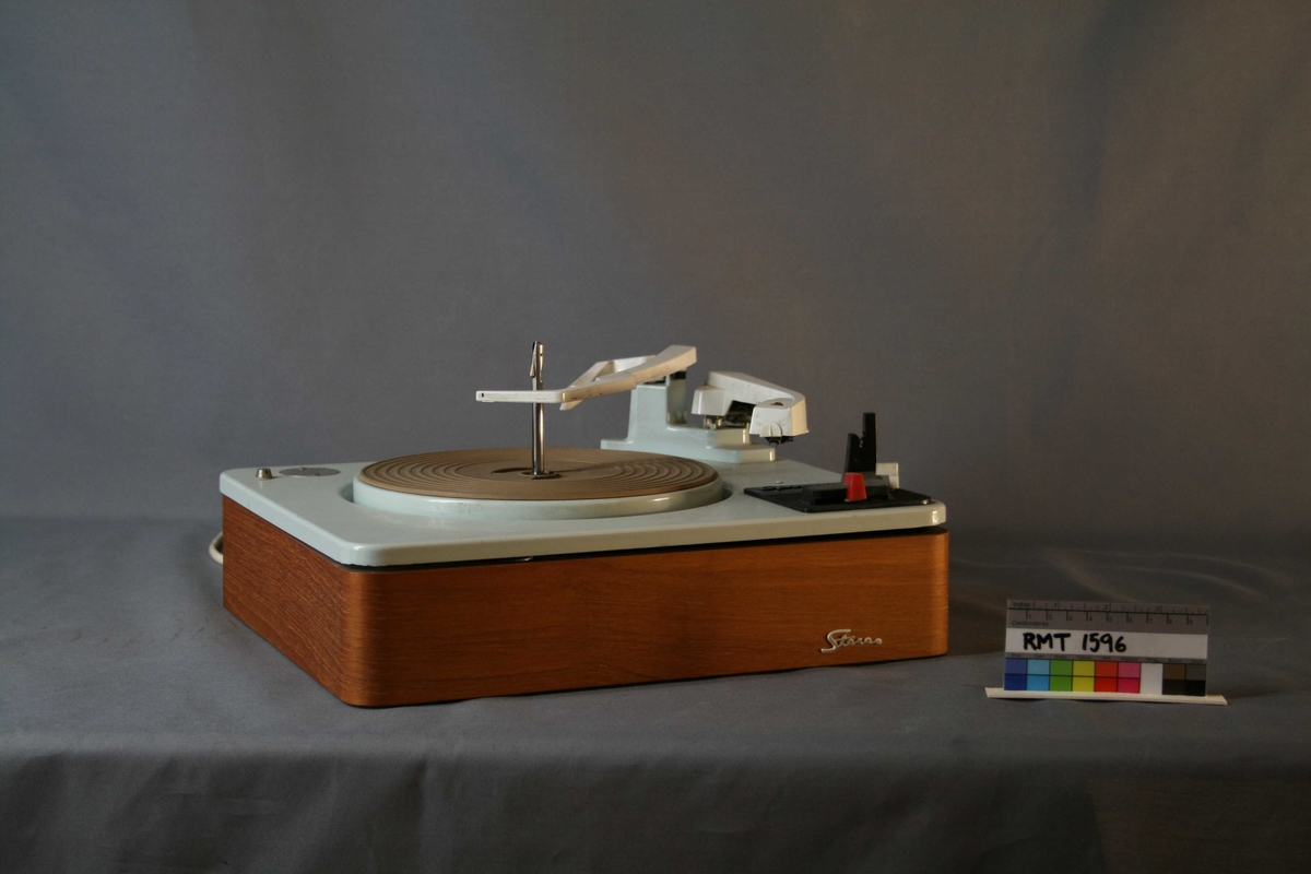 Rektangulær stereo plateskifter(spiller) for 16-, 33-, 45- og 78-plater. Lys brun kasse med lyse blått lokk. Pickuparm med stift og skiftearm. Strømuttak på baksiden.