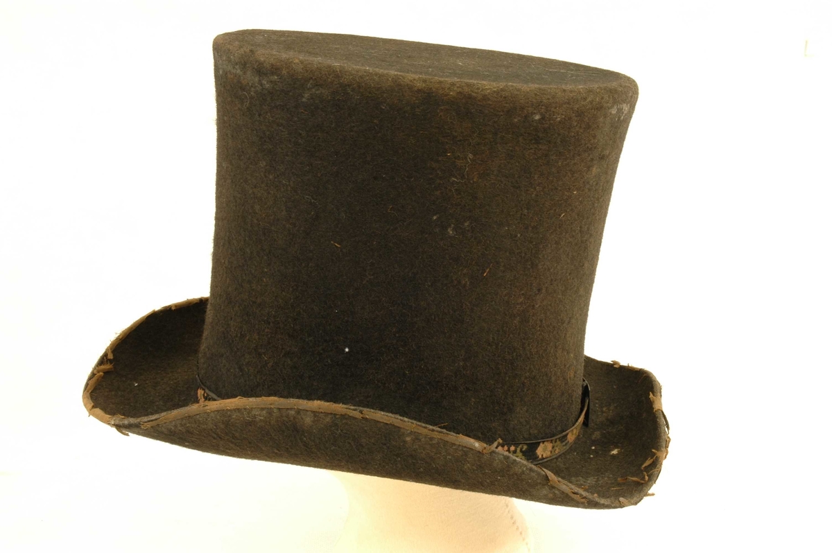Filthatten har brem og høy pull med svart blomstret band.  Hatten har innvending smal skinnkant under bremmen, og regulerbart hodeband.