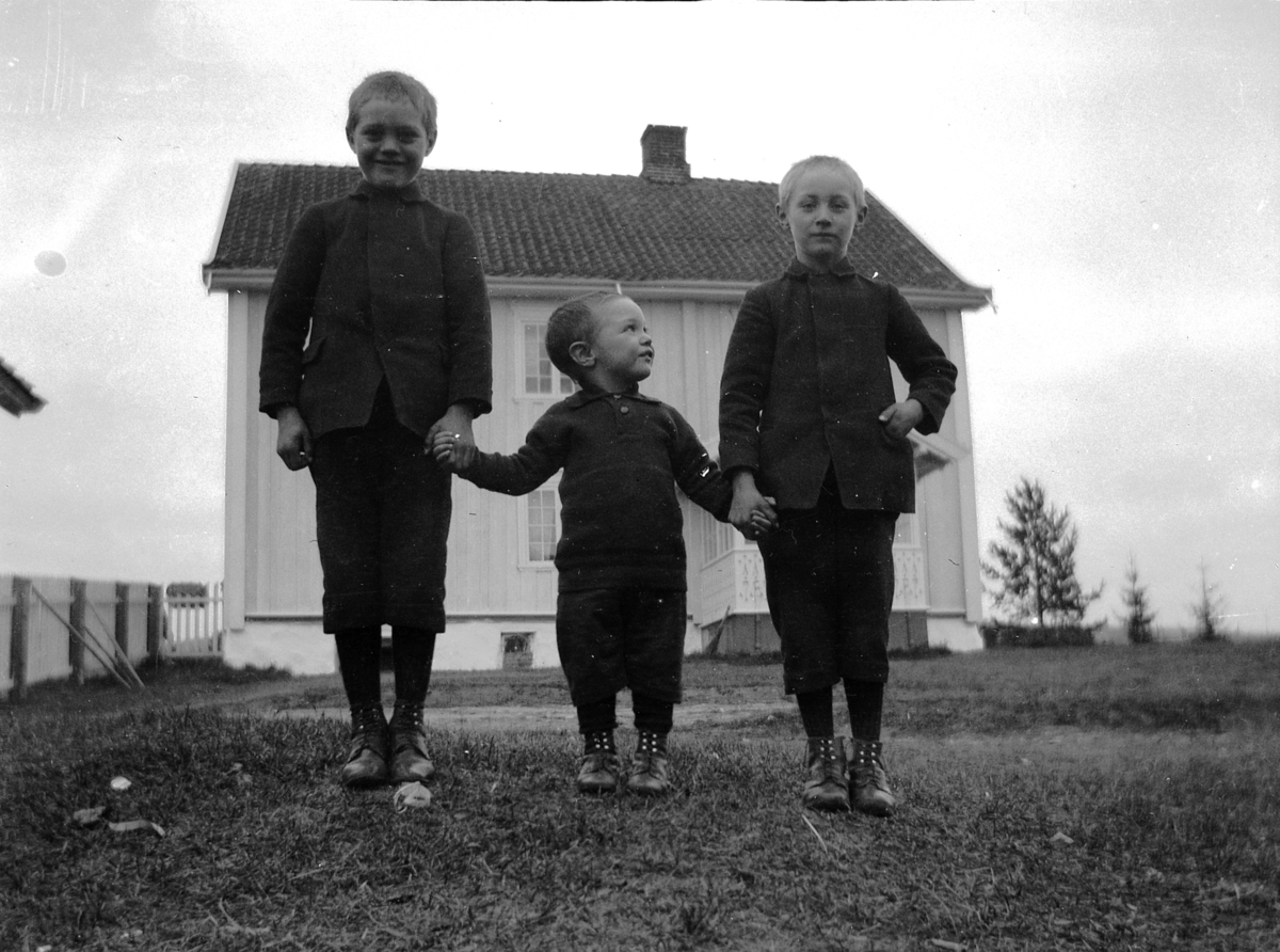 Tre gutter hånd i hånd foran hus. 