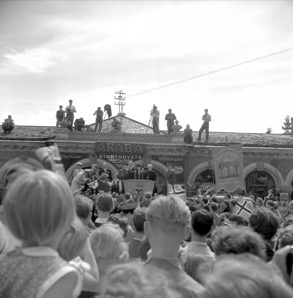 Hamar, Stortorget, signingsreisen 1958, kong Olav og prinsesse Astrid på en scene foran Basarbygningen, pressefotografer på taket,
