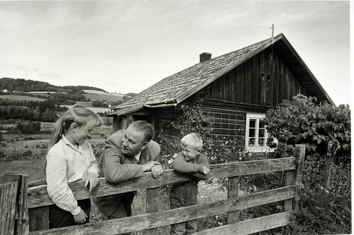 Alf Prøysen i Ringsaker i 1961, foto Johan Brun for Dagbladet, negativer på Hedmarksmuseet. 
ALF PRØYSEN, 2 BARN: MARY KRISTINE OG JAN OLAF HAGEN, GRINDA FORAN PRØYSENSTUA, RINGSAKER. FOTO: JOHAN BRUN, 1961