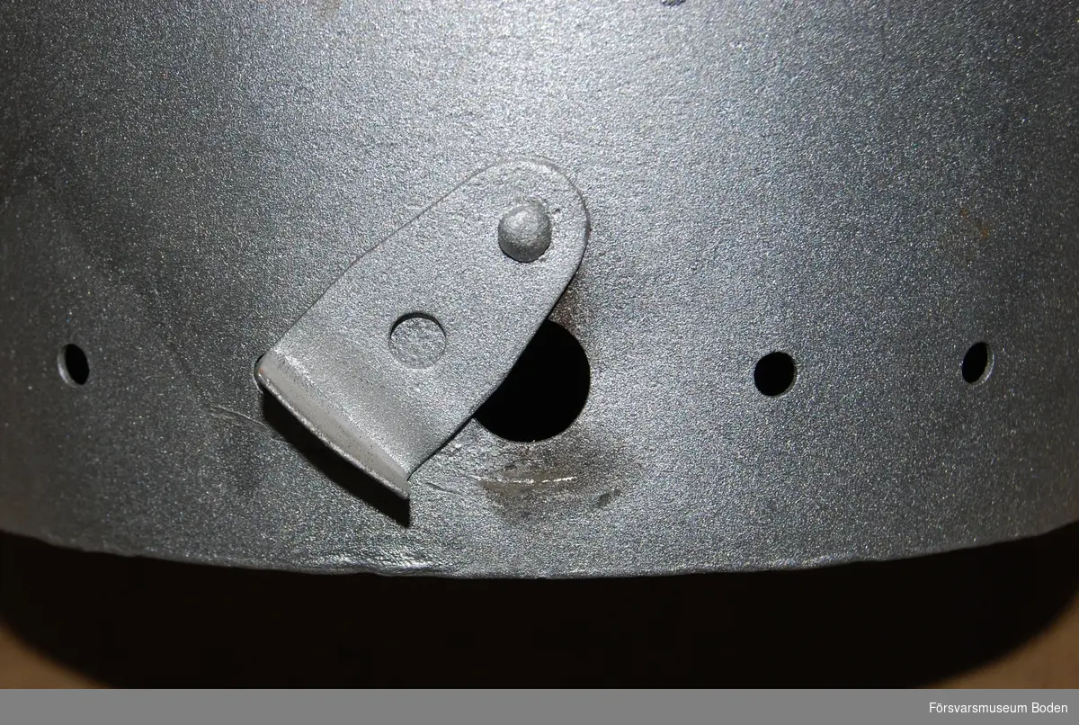 Hink av silverlackerad plåt. Locket har nätförsedd öppning. Hål runt nederkanten, där ett av dem är större och kan stängas till. Varningsskylt för kolgas på sidan.