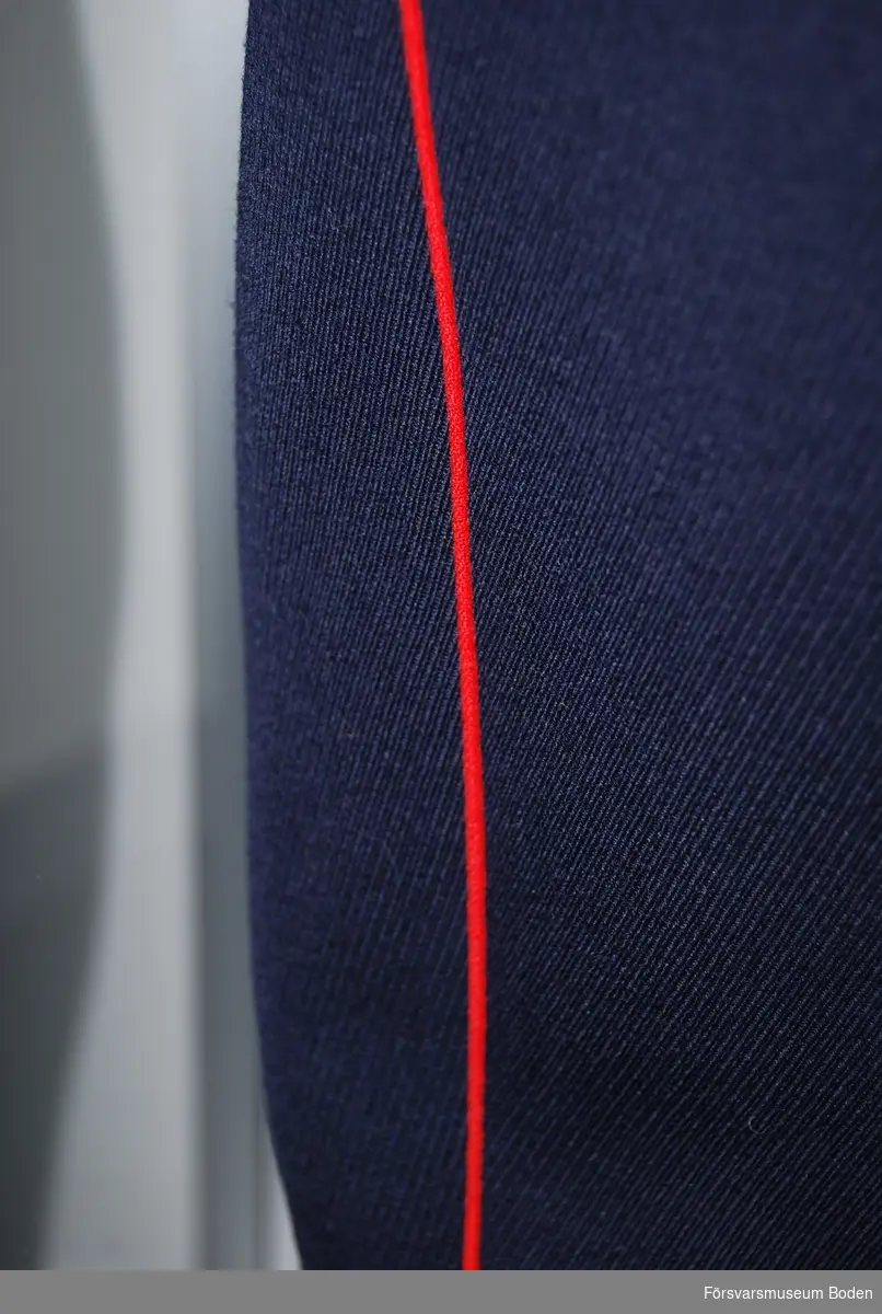 Mörkblått kläde med röda passpoaler längs yttersömmarna. Längst ner elastiska hällor runt hälen.