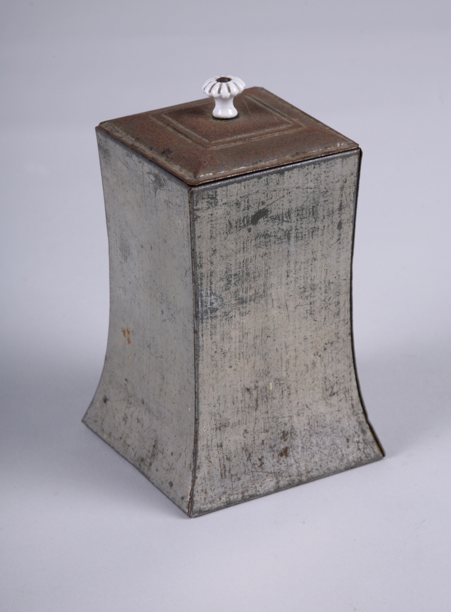 Rektangulær boks med innsvungne sider og avtagbart lokk. Lokket har en hvit blomsterformet knott av porselen.