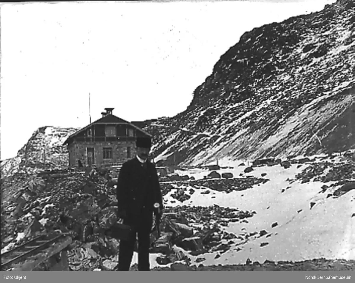 Stasjonsanlegget på Myrdal under arbeid, ferdig stasjonsbygning i bakgrunnen, en mann i forgrunnen