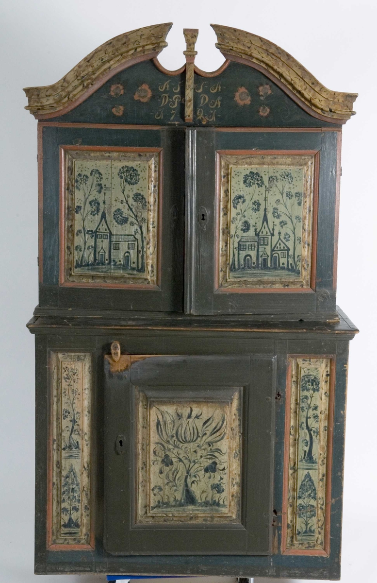 Framskap i to deler. Buet topplist. Skuffer og skjehylle i overskap. Malt innvendig og utvendig. Kirke og bygning malt på dør på overskap. Planter på underdel. Marmorert på lister på overskap.