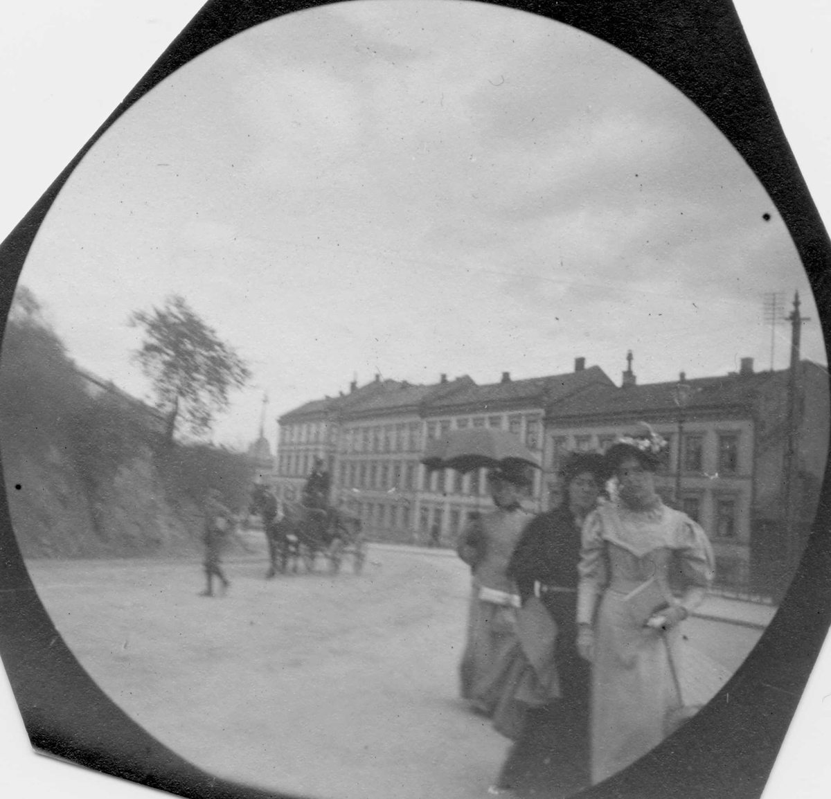 Tre kvinner spaserer i bygate, Oslo. Hestekjøretøy i gata og bygårder i bakgrunnen.