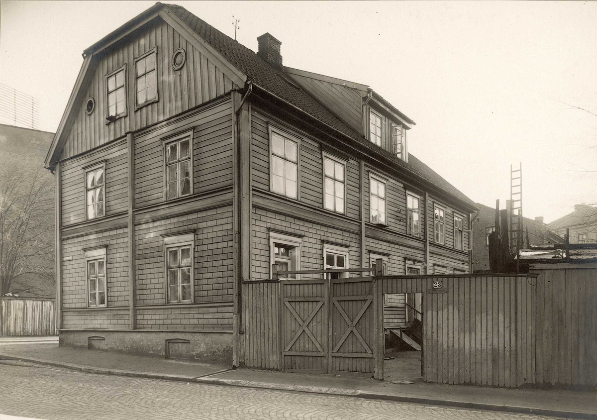 Bakkegaten 23, Oslo. Enden og baksiden av huset tatt fra gata med gjerde og port til bakgården.