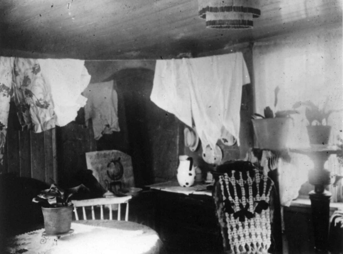 Interiør, stue, ant. Grønlandsstrøket, Oslo. Tett møblert rom med klestørk på snorer under taket. 
Fra Nanna Brochs boligundersøkelser i Oslo 1920-årene.
