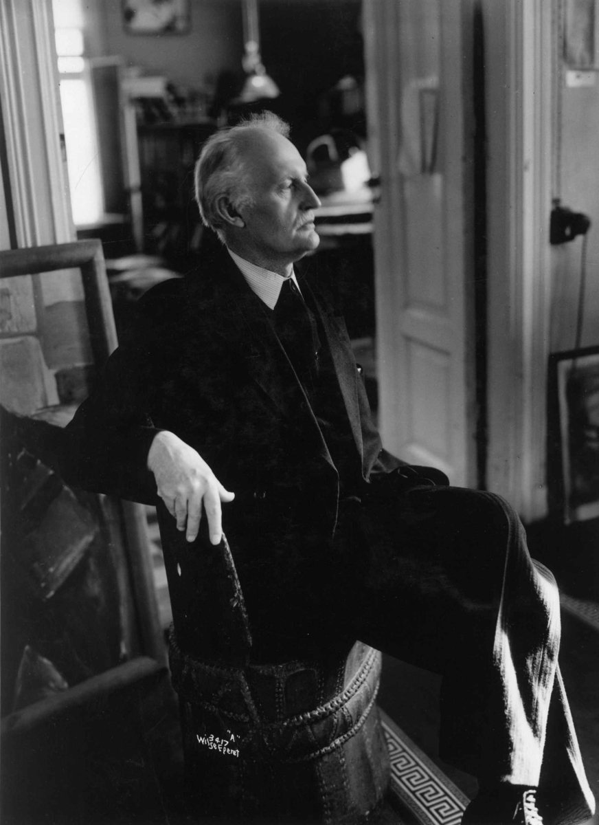 Kunstneren og maleren Edvard Munch fotografert av Anders Beer Wilse i 1937 på Ekely. Sittende i sitt atelier omgitt av sine malerier.