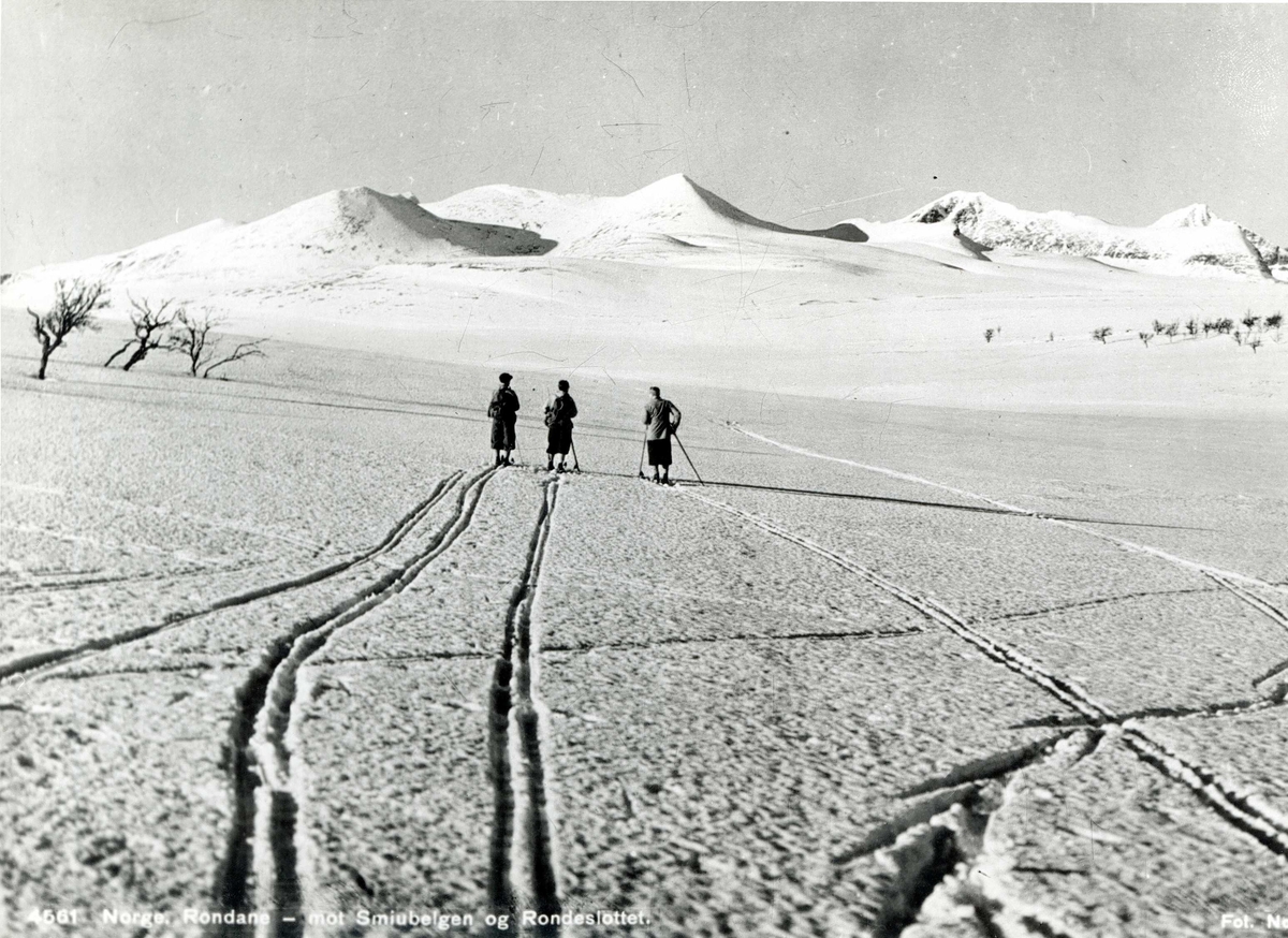 Avfotografert postkort. Tre skiløpere i Rondane. Utsikt mot Smiubelgen og Rondeslottet.