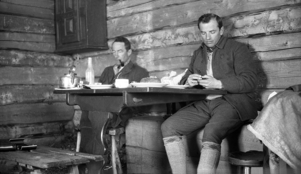 Fritjof Arentz og Sigurd Mørde sitter ved et bord i av husene på Trøan. Fotografert påsken 1929.