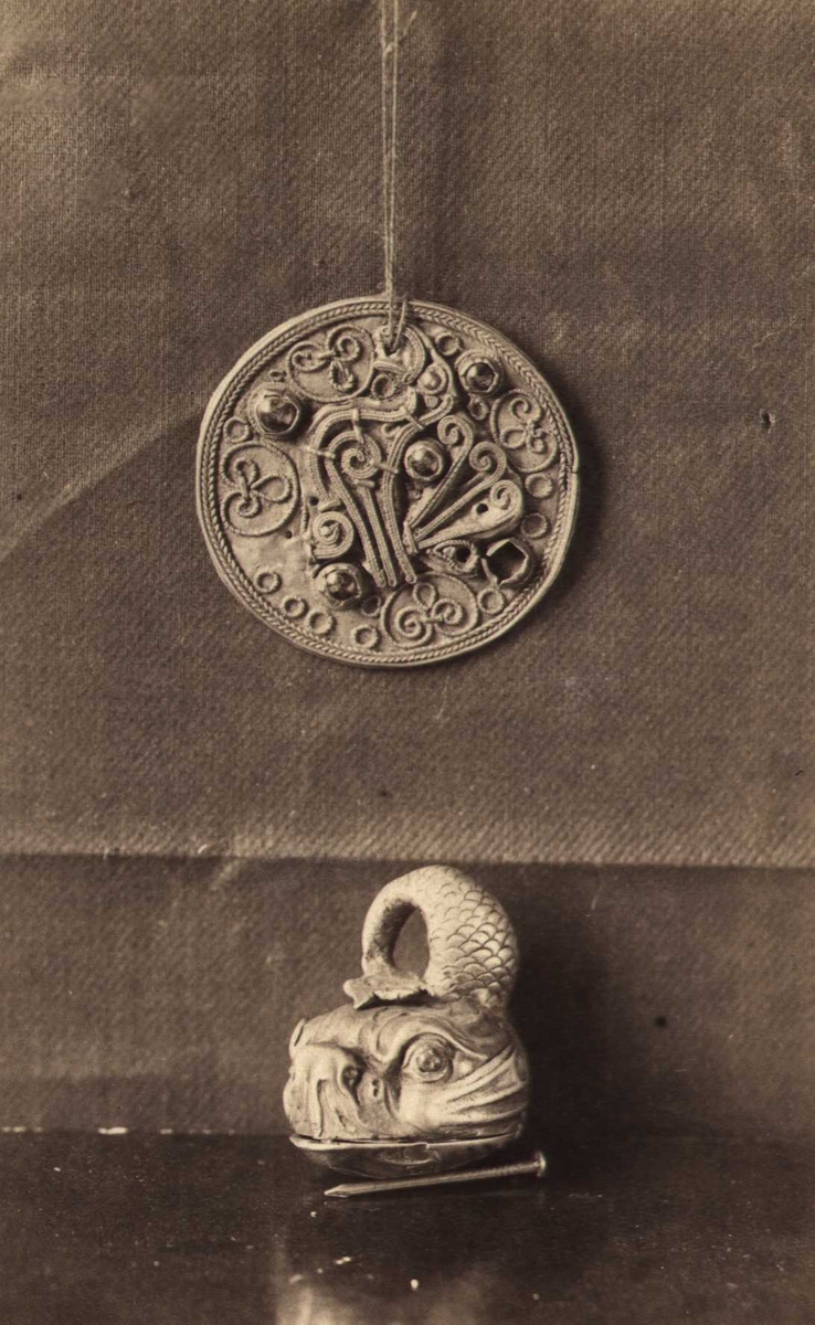 Rundt gullsmykke med drakefigur og sølvur formet som en delfin. Nå på Kunstindustrimuseet i Oslo.  