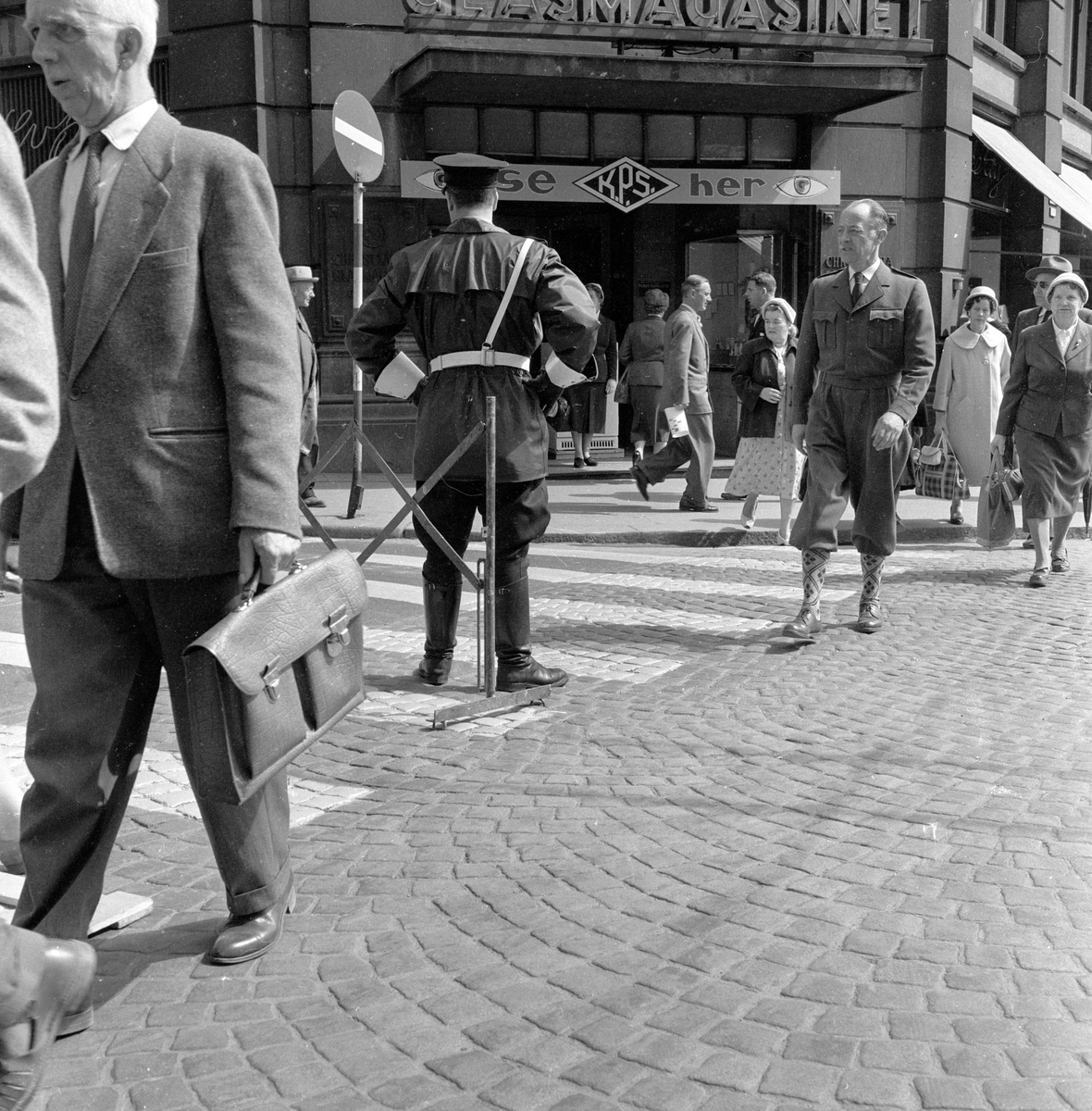 Politi passer på at fotgjengere går utenom nymalt fotgjengerfelt i krysset Møllergata og Stortorvet ved Glasmagasinet, Oslo. Fotografert mai 1959.