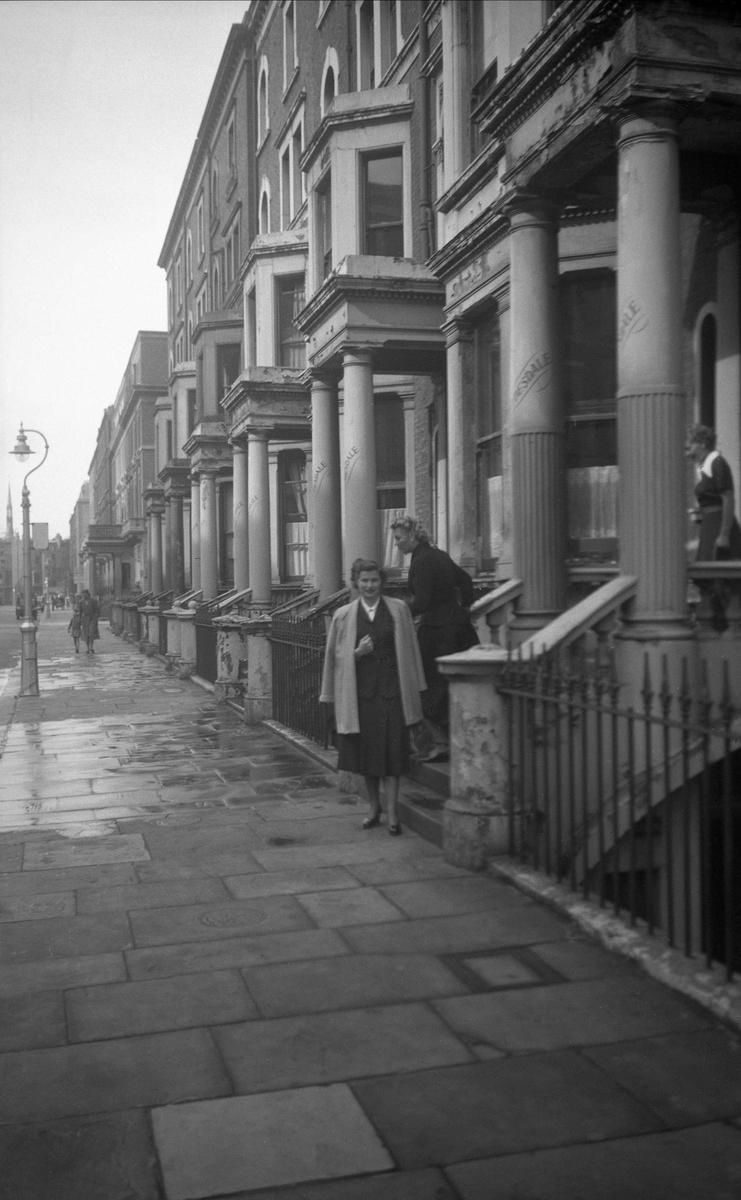 Guri Arentz ved inngangen til bygning, antagelig hotell, på Nevern Place i London. Fotografert under rundreise i Storbritannia i september 1950.